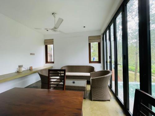 een woonkamer met een tafel, stoelen en ramen bij Leaf Olu Ella in Yatiyantota