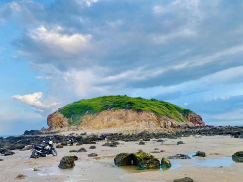 a motorcycle parked on a beach with a green hill at Homestay Nhà Của Gạo in Ấp Thiẹn Ái