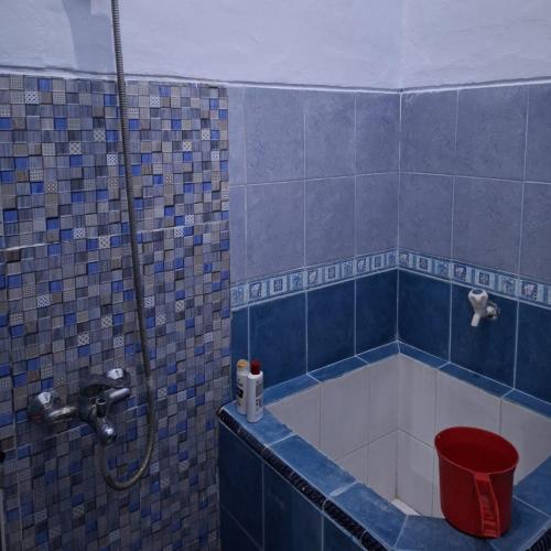a blue tiled bathroom with a shower with a red bucket at Grities 7 Home Jogja in Yogyakarta