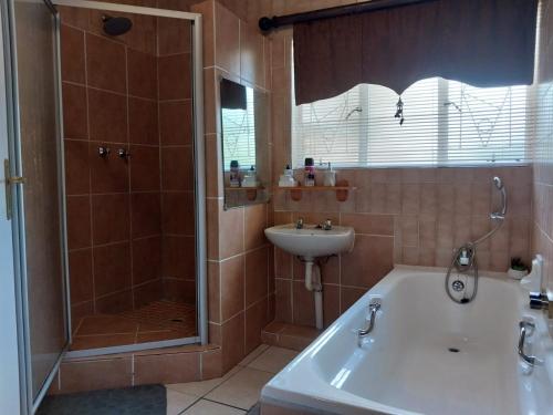 a bathroom with a shower and a tub and a sink at Lily Guesthouse in Bloemfontein