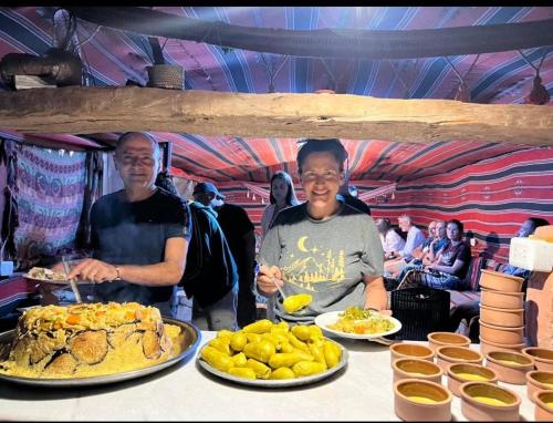 Deux hommes se tiennent debout devant une table avec des assiettes de nourriture. dans l'établissement Peace House, à Wadi Musa