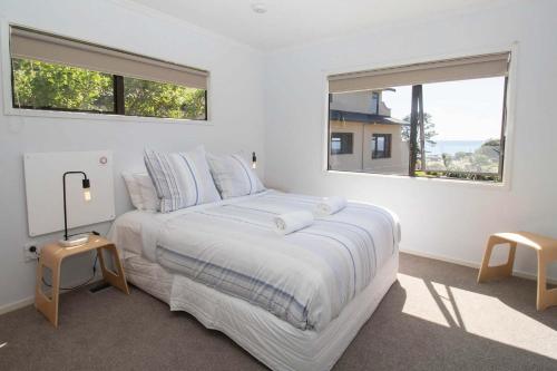 a white bedroom with a large bed with two windows at Aqua Vista On Arden - beachfront bach in Oakura in Oakura