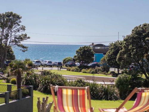 two chairs sitting on the grass near the ocean at Aqua Vista On Arden - beachfront bach in Oakura in Oakura