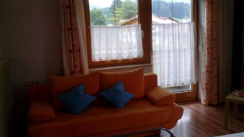 ein orangefarbenes Sofa mit blauen Kissen in einem Zimmer mit Fenstern in der Unterkunft Haus Hämmerle in Reutte