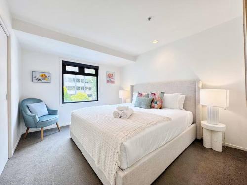 Un dormitorio blanco con una cama y una silla azul. en Prime CBD Location- Walk to Spark Area & Queen St, en Auckland