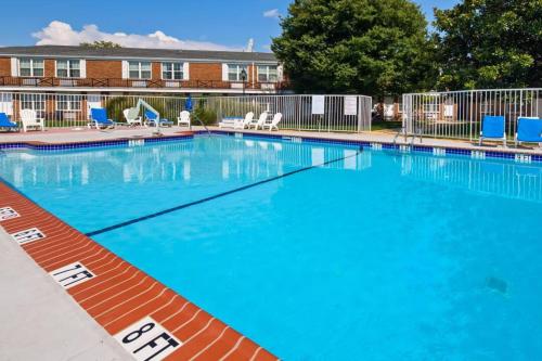 a large blue swimming pool with blue chairs and a building at Clarion Inn Falls Church-Arlington in Falls Church