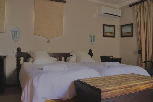 two beds with white sheets and a bench in a bedroom at Grünau Chalets in Khomas Region