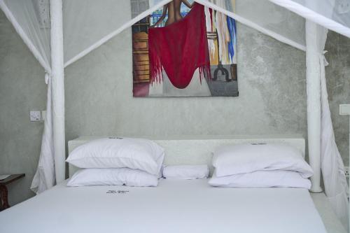 a white bed with two pillows and a painting on the wall at White Villa Paparemo Village in Watamu