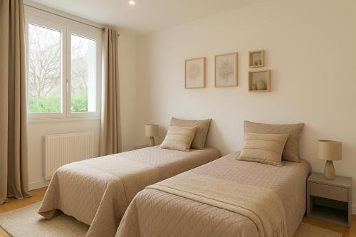 two beds in a white room with a window at La Grande Maison Paris Sud in Vitry-sur-Seine