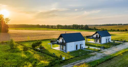 ヤヌシュコボにあるCztery Pory Rokuの太陽を背景にした野原にある2軒の家