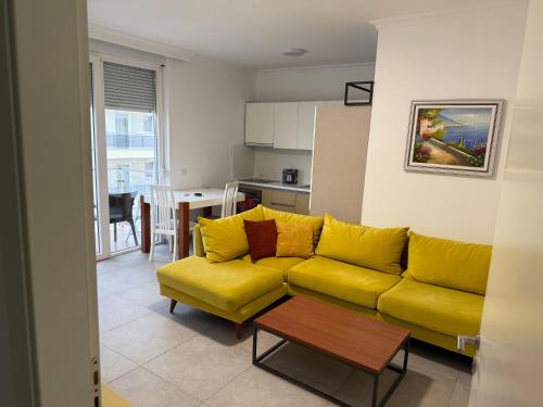 een woonkamer met een gele bank en een keuken bij Home holiday kozmai in Shëngjin