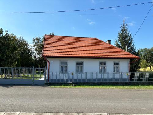 a white house with an orange roof and a fence at Gólyafészek Vendégház in Szécsény