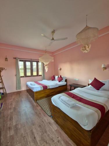 Duas camas num quarto com paredes cor-de-rosa e pisos em madeira em Hotel Tree Tops- A Serene Friendly Hotel in Sauraha em Chitwan