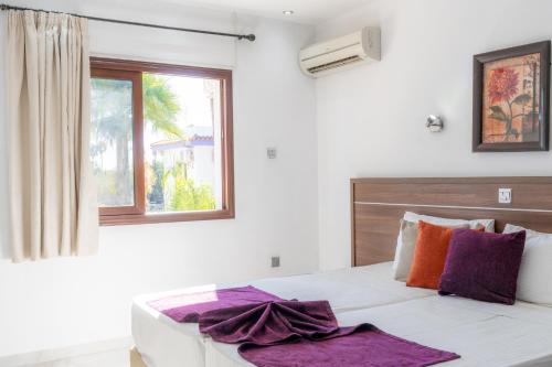 a bedroom with a bed with purple pillows and a window at Amethyst Napa Annex Apartments in Ayia Napa