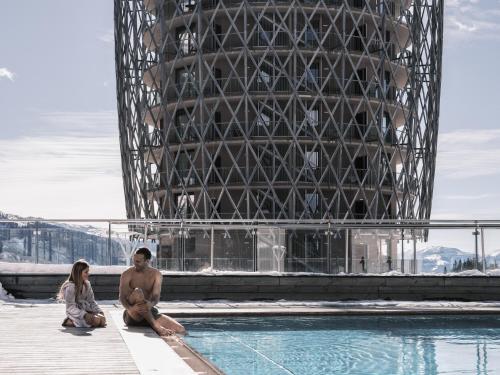 a man and a woman sitting next to a swimming pool at Falkensteiner Aktiv & Familienhotel Cristallo Superior in Katschberghöhe