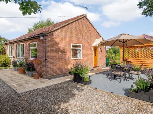 a brick cottage with a table and an umbrella at Paddock End in Great Plumstead