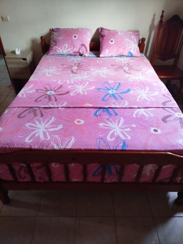een bed met een roze sprei met bloemen erop bij le petit couin des voyageurs in Bouillante