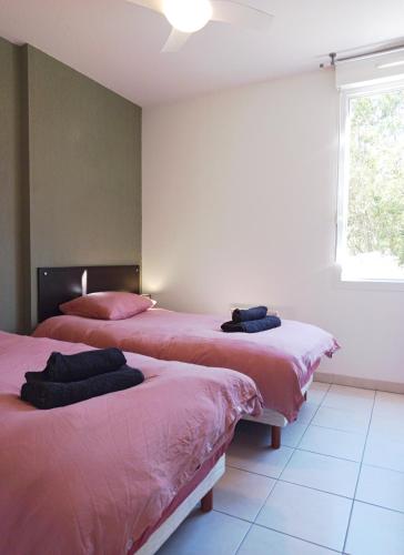 two beds in a room with pink sheets and a window at Le Chant des Cigales in Azille