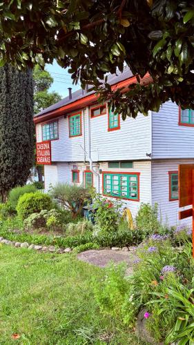 a white building with green windows and a sign at Cabañas Casona Italiana in Lago Ranco