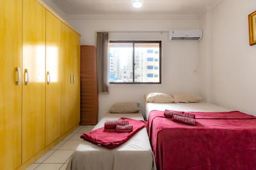 a bedroom with two beds with red sheets and a window at Apartamento com Varanda, Churrasqueira e Vista Mar in Meia Praia