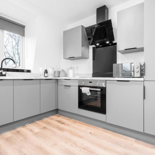 a white kitchen with white appliances and a wooden floor at Modern Two Bed Apartment - Balcony & Parking - Netflix 8MC in Birmingham
