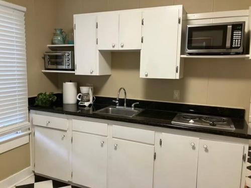 a kitchen with white cabinets and a sink and a microwave at Bright 1BR Hideaway Close to UL Lafayette in Lafayette