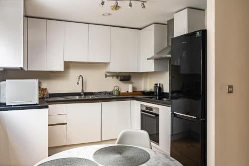 a kitchen with white cabinets and a black refrigerator at Stylish Greenwich Apartment with Balcony And River Views in London
