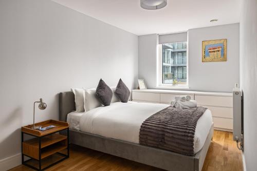 a white bedroom with a large bed and a window at Stylish Greenwich Apartment with Balcony And River Views in London