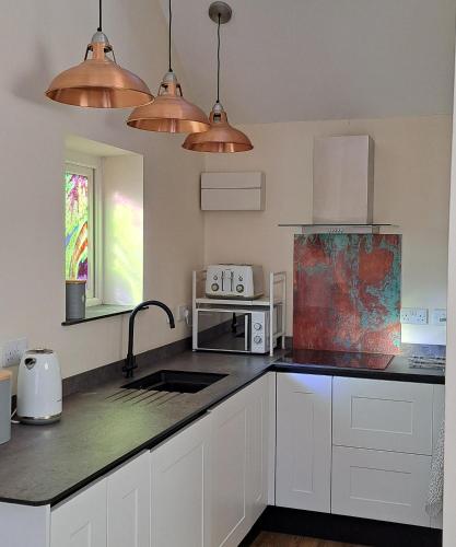 a kitchen with white cabinets and copper pendant lights at Ty Heulwen Studio in St. Davids