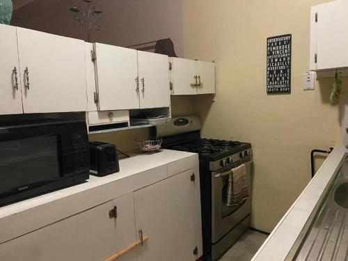 a kitchen with white cabinets and a stove and a microwave at charming 1 bedroom house in Port-of-Spain
