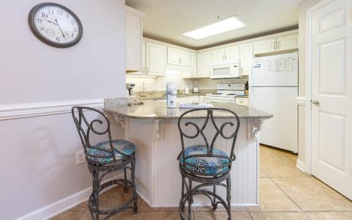 Phoenix X 1412 condo في شاطئ أورانج: مطبخ مع كونتر مع كرسيين وساعة