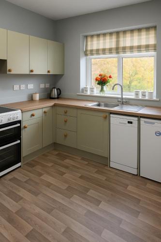 cocina con armarios blancos y suelo de madera en The Holm, en Canonbie