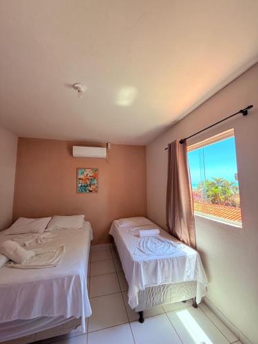 two beds in a room with a window at Casa Temporada Suítes in Maragogi