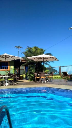 a swimming pool with umbrellas and a table and chairs at Pousada DiMari in Boicucanga