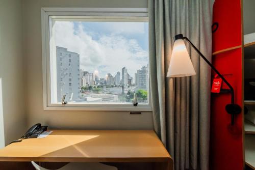 a desk in a room with a window and a lamp at ibis Navegantes Itajai in Itajaí