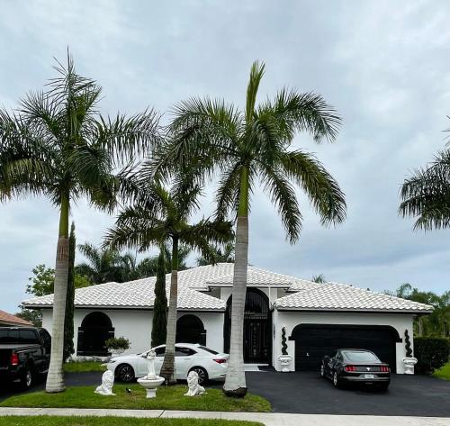 a house with two palm trees in front of it at Lux 4 bedroom home on lake with pool! in Coral Springs