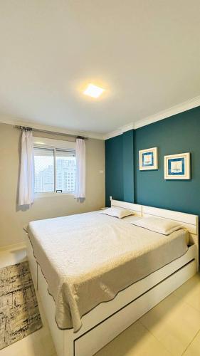 a bedroom with a large bed with a blue wall at Apartamento Guarujá, com sacada vista mar! Pé na areia, Lindo! in Guarujá