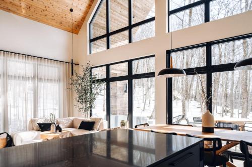 a living room with large windows and a table at Le coup de coeur du Lac Supérieur - 3 minutes from Tremblant! in Lac-Superieur