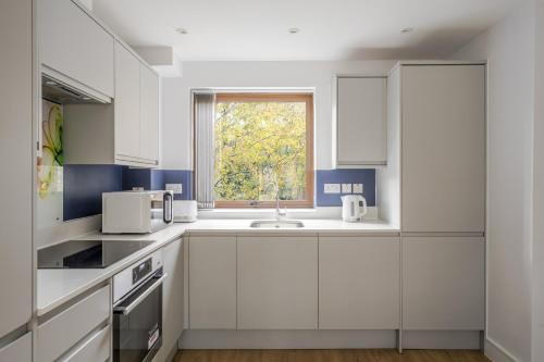 a kitchen with white cabinets and a window at Premium Apartment in Chelmsford City, Free WiFi & Free Parking - Dukes Apartment by Stays Accommodation - Long Stays Welcome in Chelmsford