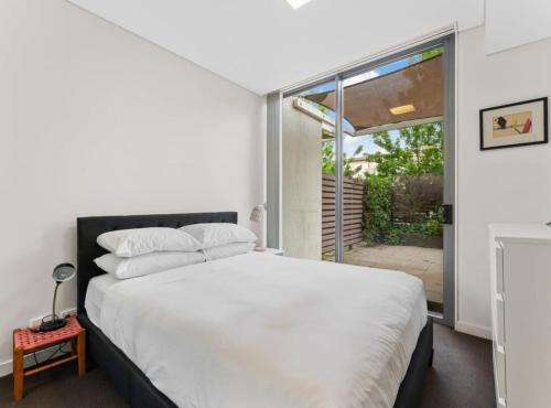 een slaapkamer met een wit bed en een glazen schuifdeur bij Tranquil 1-Bed Apartment with Courtyard, Pool, BBQ in Phillip