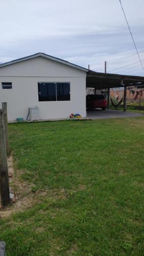 a white house with a green yard with a car at Casa de Veraneio in Passo De Torres