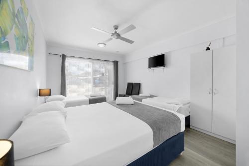 a white bedroom with two white beds and a window at Pacific Paradise Airport Motel in Pacific Paradise 