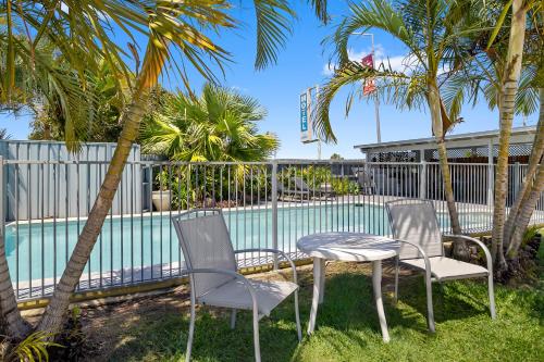 three chairs and a table next to a swimming pool at Pacific Paradise Airport Motel in Pacific Paradise