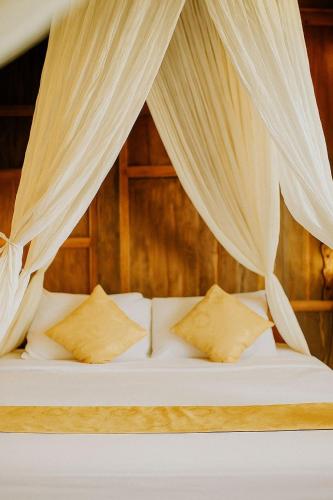 - un lit avec des rideaux et des oreillers blancs dans l'établissement Kalyana Gangga, à Krambitan