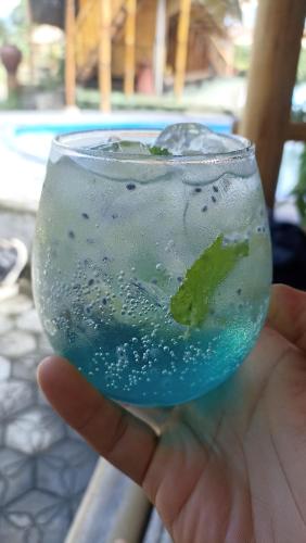 a hand holding a glass with a blue drink at Penempuran cottage in Masbagik