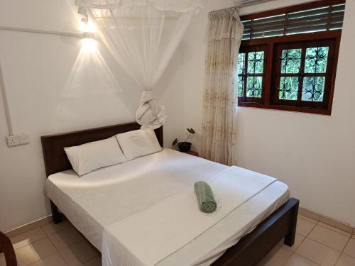 a bedroom with a large bed with white sheets and a window at Coco Mango Hostel in Dickwella
