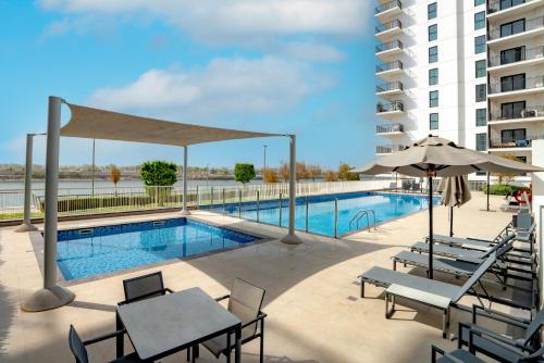 a swimming pool with tables and chairs next to a building at Modern 1-Bed Apartment with Balcony & Free Parking l Near Yas Mall & F1 Yas Island & Sea world in Abu Dhabi