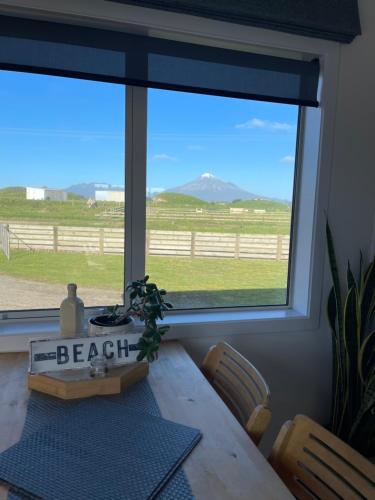 a dining room table with a view of a pasture through a window at The Blue Bach in Opunake