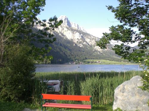 a red bench in front of a lake with a mountain at Almdorf Tirol in Haldensee
