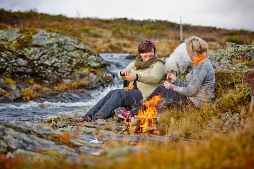 zwei Frauen und ein Hund sitzen um ein Feuer in der Unterkunft Storefjell Resort in Gol